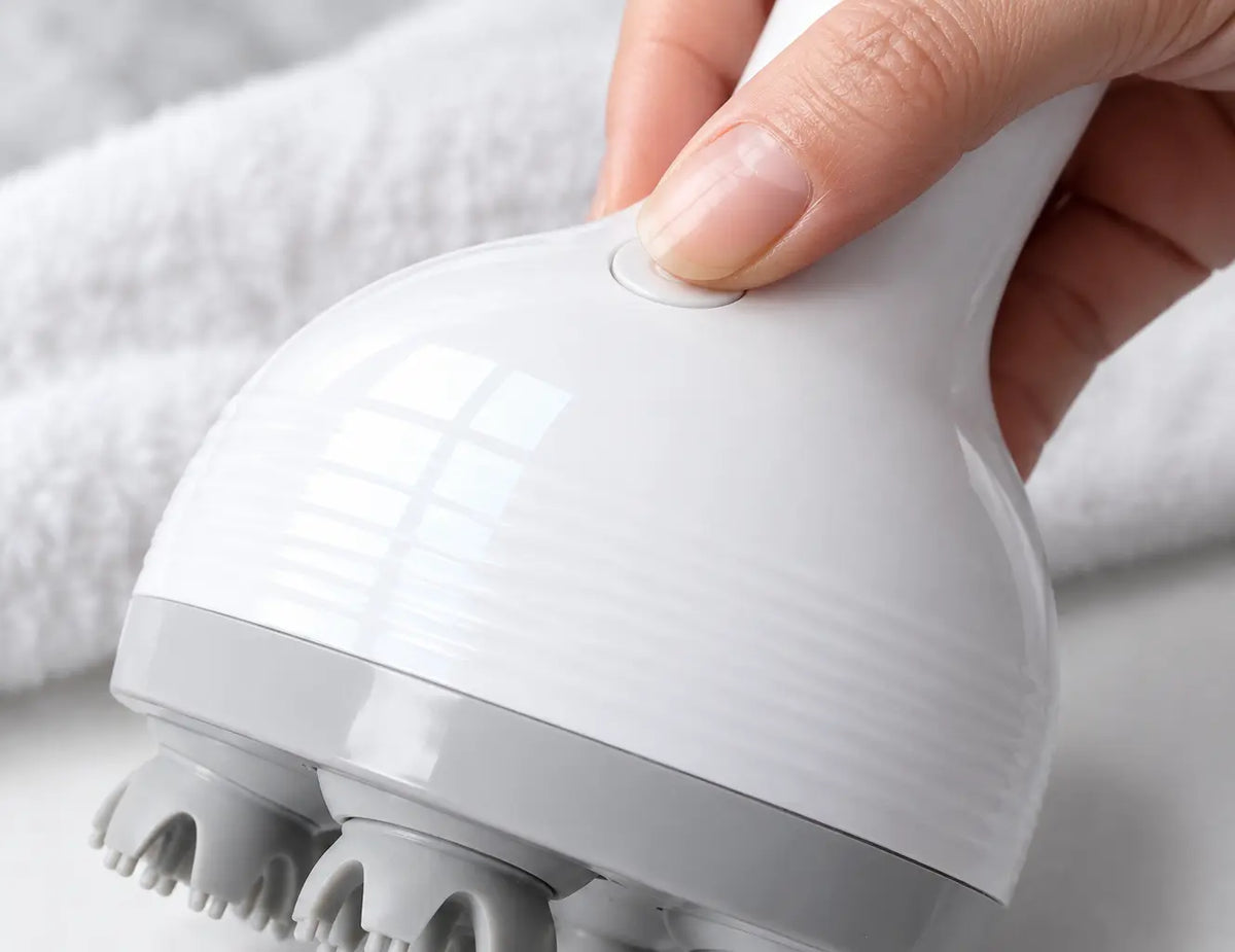 A close detail photograph of the exact Nuage scalp massager from the reference at the moment a thumb